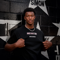 Model in the black Meant To Be Tee, front, MEANT2B chest print in pink and white against a star mural