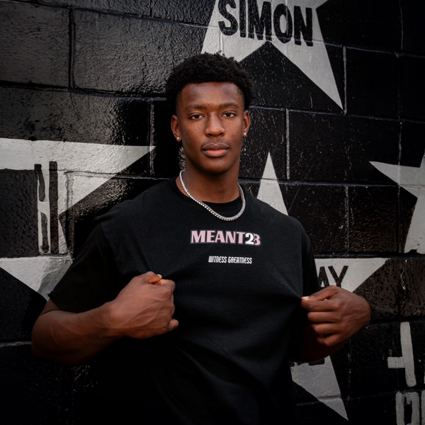 Model in the black Meant To Be Tee, front, MEANT2B chest print in pink and white against a star mural